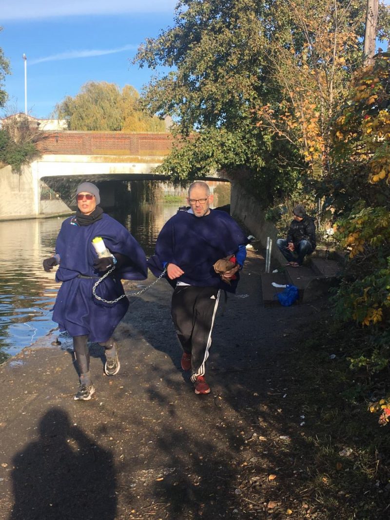 Image shows Ellen Cottom and the Boyf running chained at the wrist wearing blanket ponchos