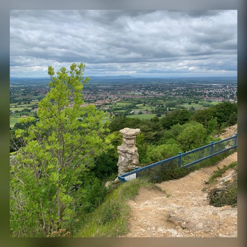 Stone stack known as the Devil's Chimney with Cheltenham and the Malvern Hills visible in the background